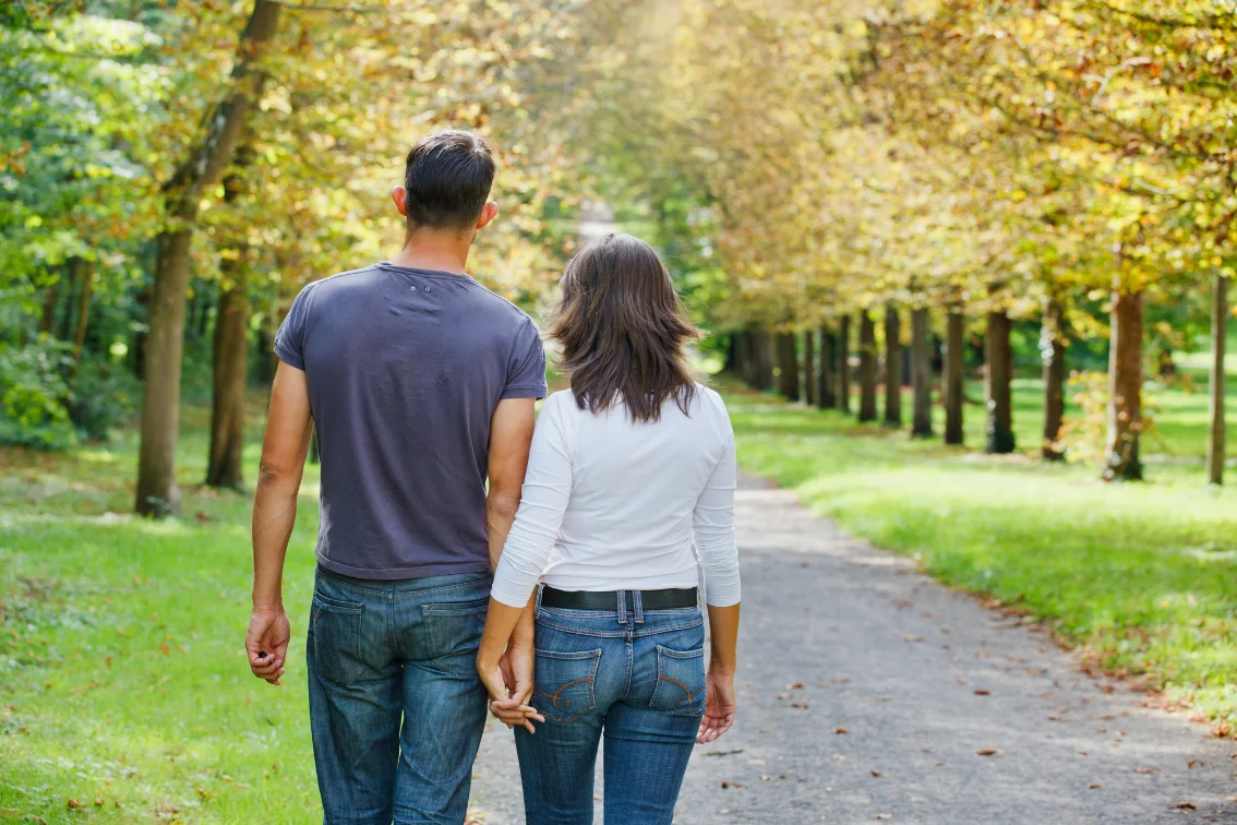 A couple walking hand in hand along a tree-lined path in autumn