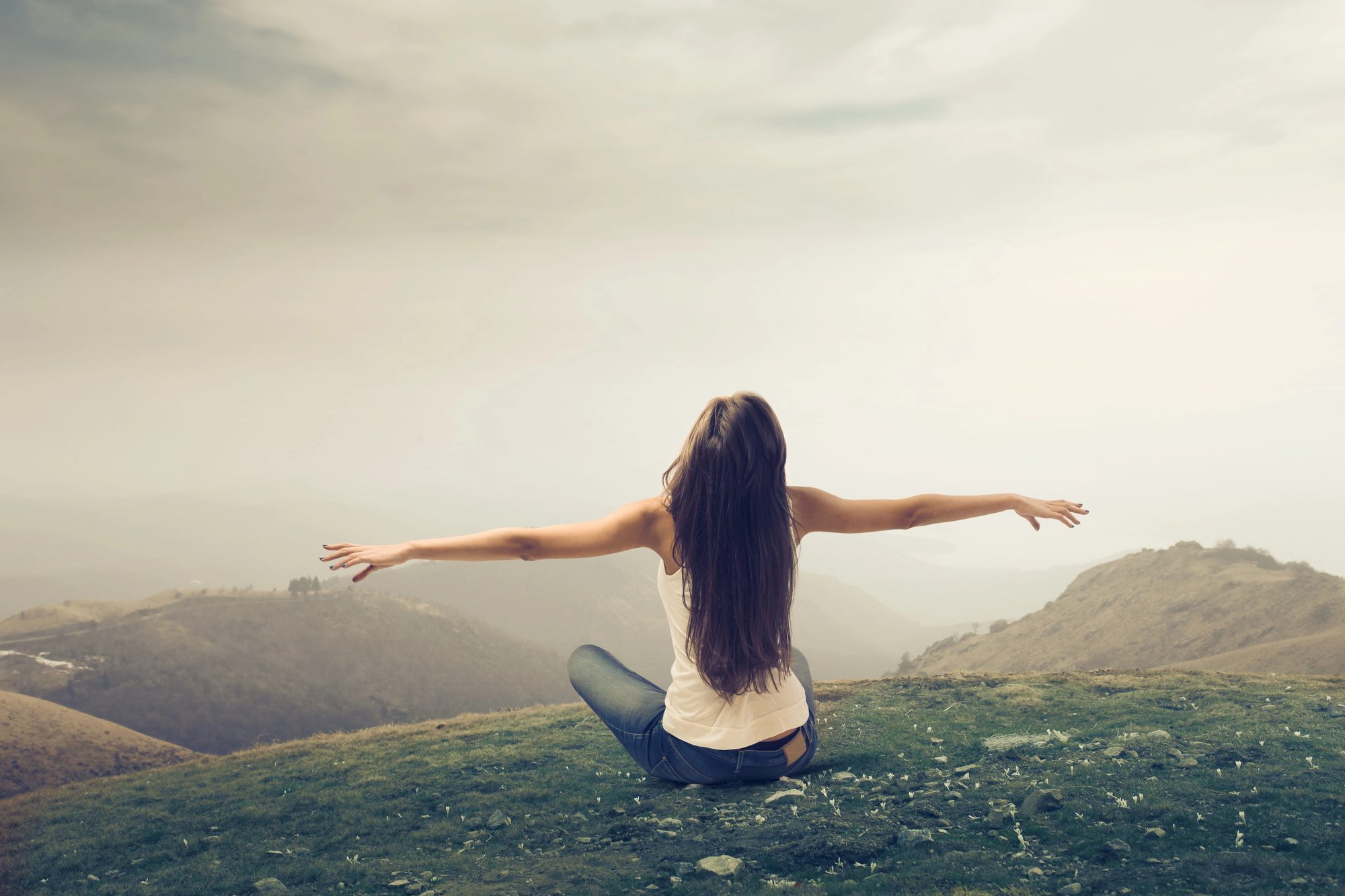 A person sitting on a hillside with arms outstretched, representing wellness and calm