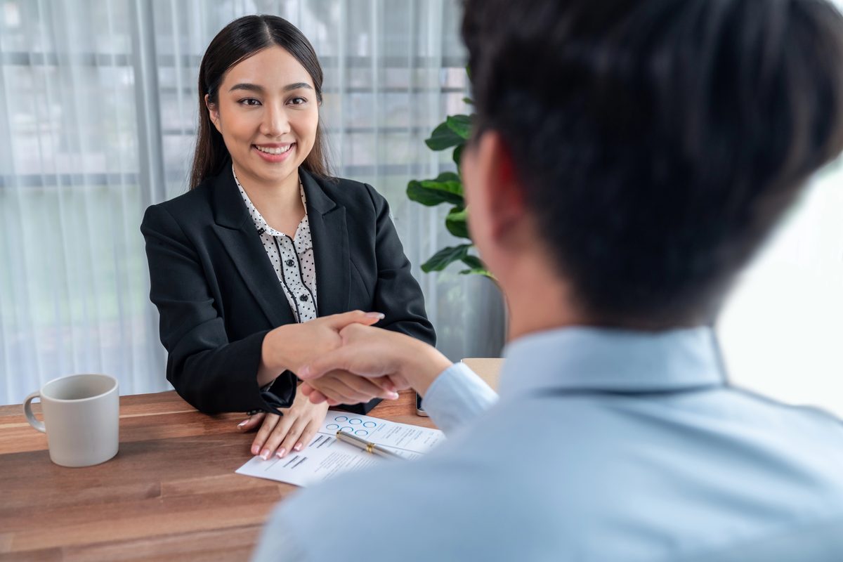 Two professionals shaking hands across a desk during a business meeting