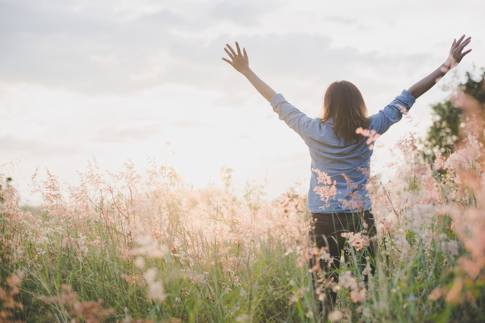 Woman standing in a sunlit meadow with her arms raised
